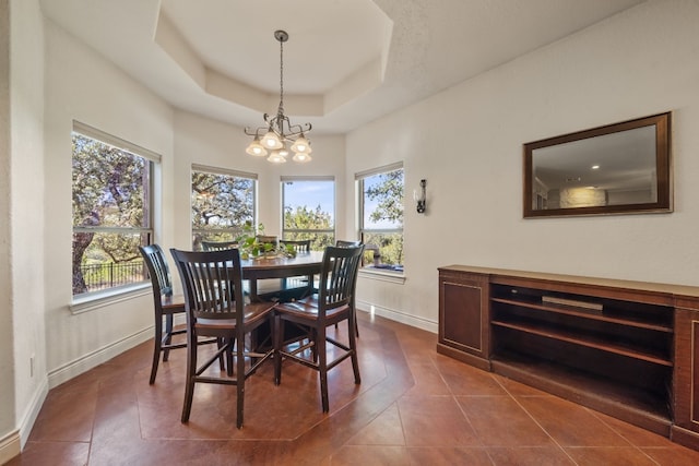 dining room with dark tile patterned flooring, a notable chandelier, a healthy amount of sunlight, and a raised ceiling