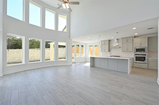7701 Becasseau Dr, Austin, TX 78738 - kitchen featuring appliances with stainless steel finishes, wall chimney range hood, gray cabinets, open floor plan, and a high ceiling