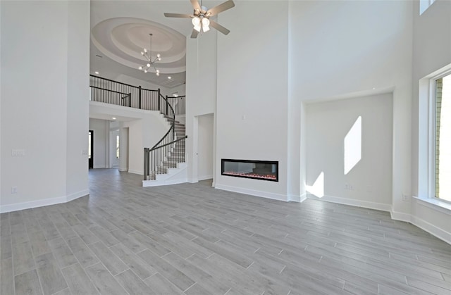 7701 Becasseau Dr, Austin, TX 78738 - unfurnished living room with a towering ceiling, stairs, light wood-type flooring, a tray ceiling, and a ceiling fan