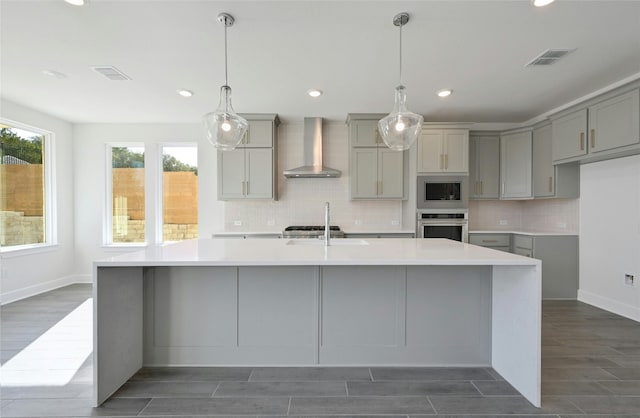 7701 Becasseau Dr, Austin, TX 78738 - kitchen featuring wall chimney range hood, gray cabinets, appliances with stainless steel finishes, tasteful backsplash, and wood finish floors