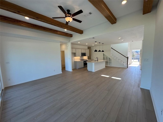 unfurnished living room with beamed ceiling, ceiling fan, light wood-type flooring, and sink