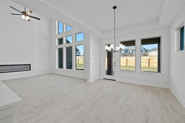 interior space featuring ceiling fan with notable chandelier, light hardwood / wood-style floors, and a raised ceiling