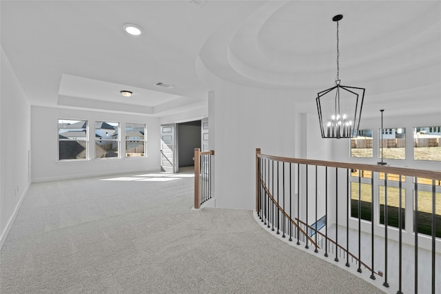 hallway featuring a raised ceiling, light carpet, and a notable chandelier