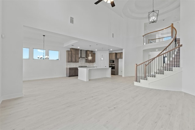 unfurnished living room with ceiling fan, light hardwood / wood-style floors, a raised ceiling, and a towering ceiling