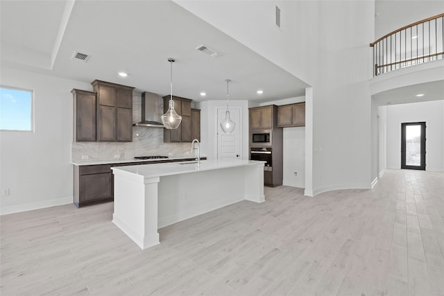 kitchen with wall oven, built in microwave, a kitchen island with sink, and wall chimney range hood