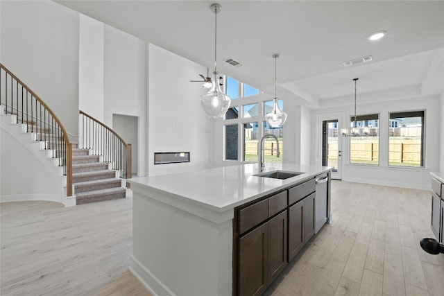 kitchen with dark brown cabinetry, sink, dishwasher, a notable chandelier, and a kitchen island with sink