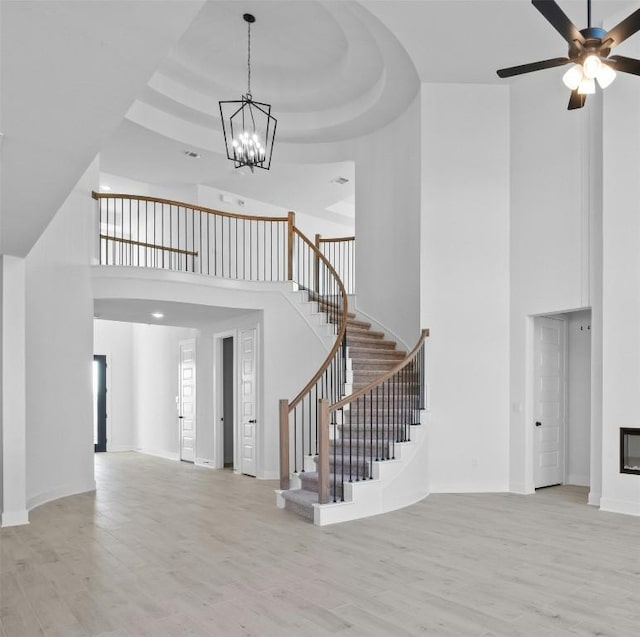 foyer featuring a raised ceiling, a towering ceiling, light hardwood / wood-style floors, and ceiling fan with notable chandelier