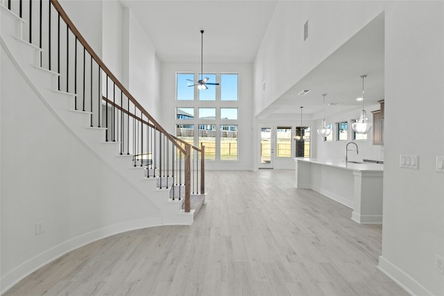 entrance foyer with ceiling fan, sink, a towering ceiling, and light wood-type flooring