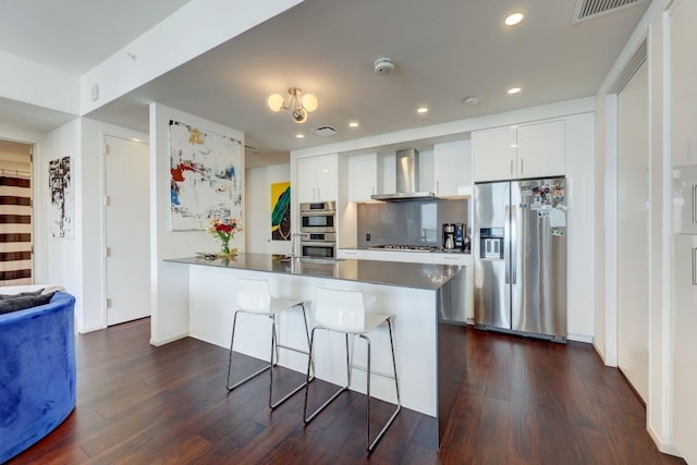 kitchen featuring wall chimney range hood, stainless steel appliances, white cabinets, and a kitchen bar