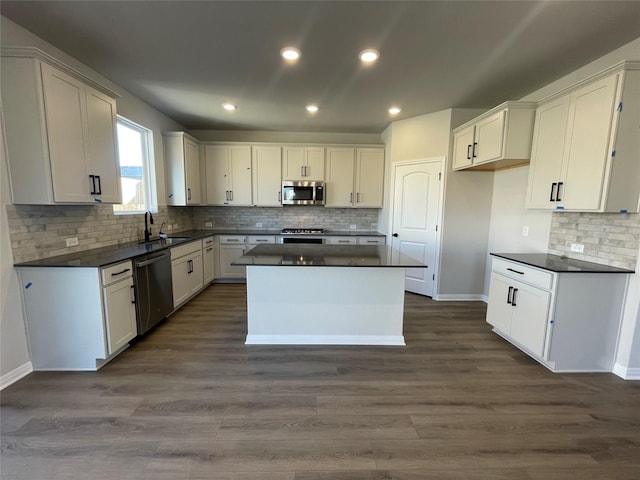 kitchen with white cabinets, appliances with stainless steel finishes, a kitchen island, dark hardwood / wood-style flooring, and sink