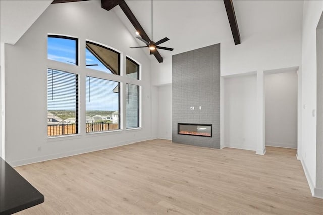 unfurnished living room with beamed ceiling, ceiling fan, a fireplace, and light hardwood / wood-style flooring