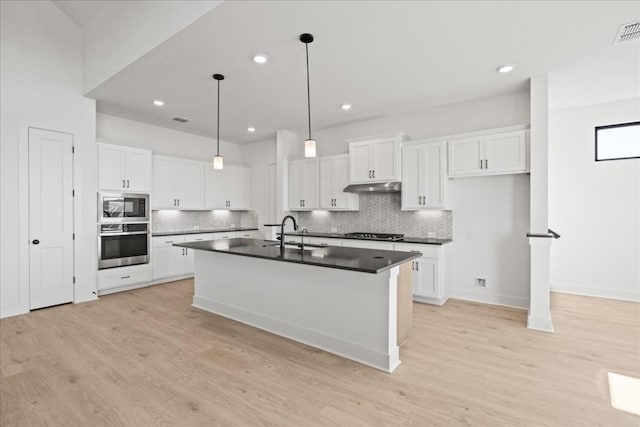 kitchen featuring built in microwave, white cabinetry, stainless steel oven, sink, and a center island with sink