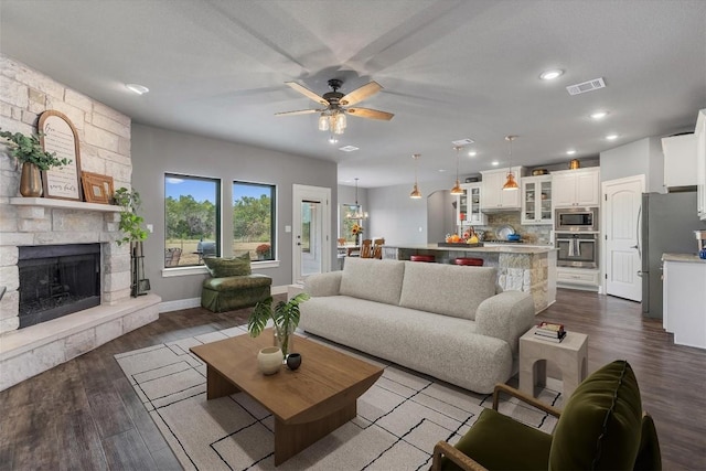 living room with a stone fireplace, ceiling fan with notable chandelier, and dark hardwood / wood-style flooring