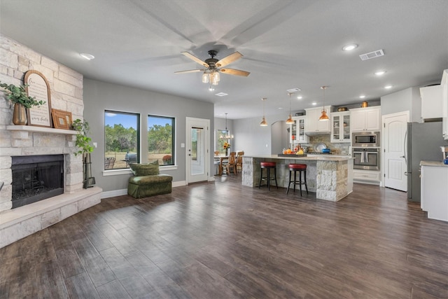 unfurnished living room with dark wood-type flooring, ceiling fan with notable chandelier, and a stone fireplace