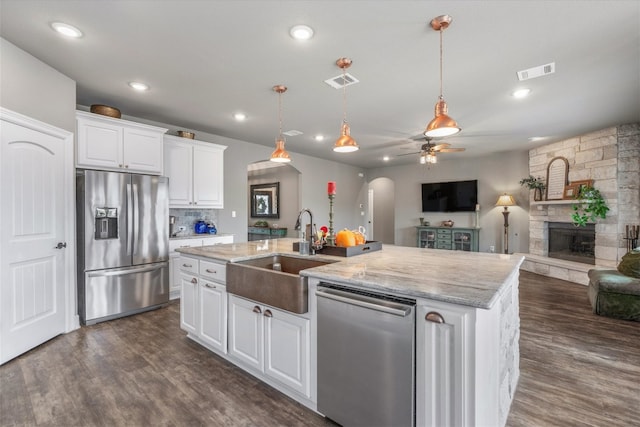 kitchen featuring a center island with sink, white cabinets, sink, a fireplace, and appliances with stainless steel finishes