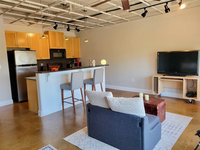 kitchen featuring stainless steel fridge, light brown cabinetry, decorative light fixtures, a kitchen bar, and kitchen peninsula