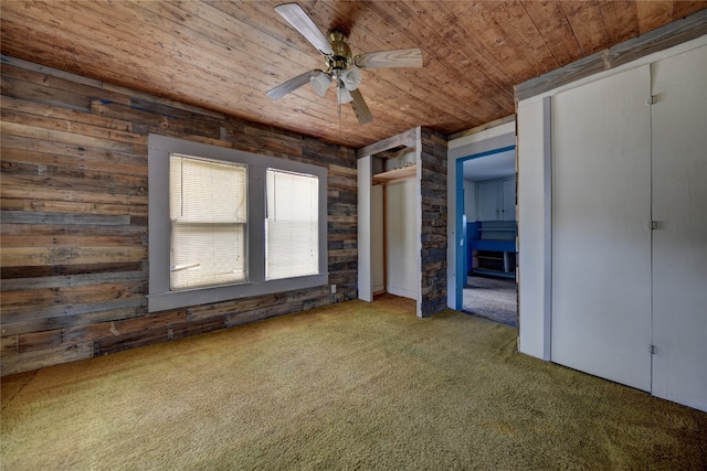 unfurnished bedroom featuring carpet flooring, wooden walls, ceiling fan, and wooden ceiling