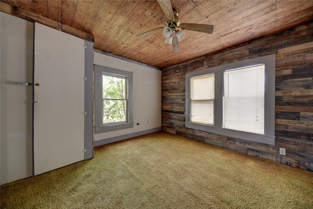 carpeted spare room featuring wood walls, ceiling fan, and wood ceiling