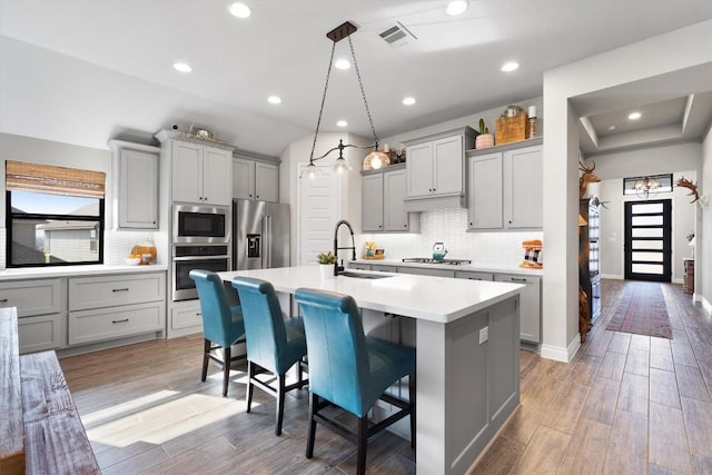 kitchen featuring gray cabinetry, sink, stainless steel appliances, a kitchen bar, and a kitchen island with sink