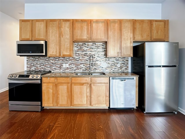 kitchen with tasteful backsplash, appliances with stainless steel finishes, sink, dark wood-type flooring, and dark stone countertops