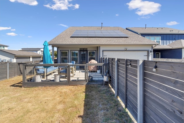 rear view of property featuring solar panels, a garage, and a yard