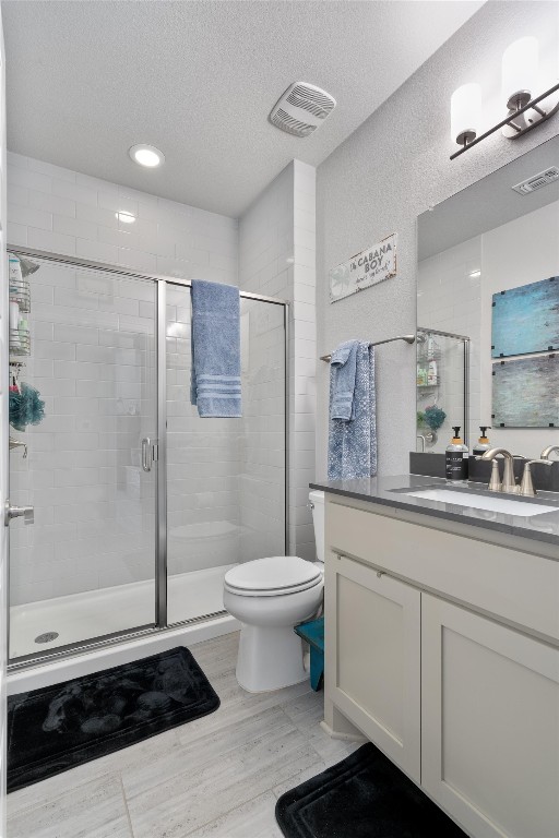 bathroom featuring vanity, a textured ceiling, an enclosed shower, hardwood / wood-style floors, and toilet