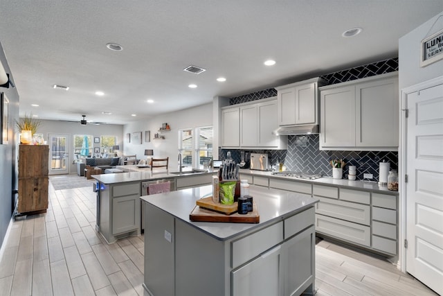 kitchen with gray cabinetry, a kitchen island, light wood-type flooring, stainless steel gas cooktop, and ceiling fan