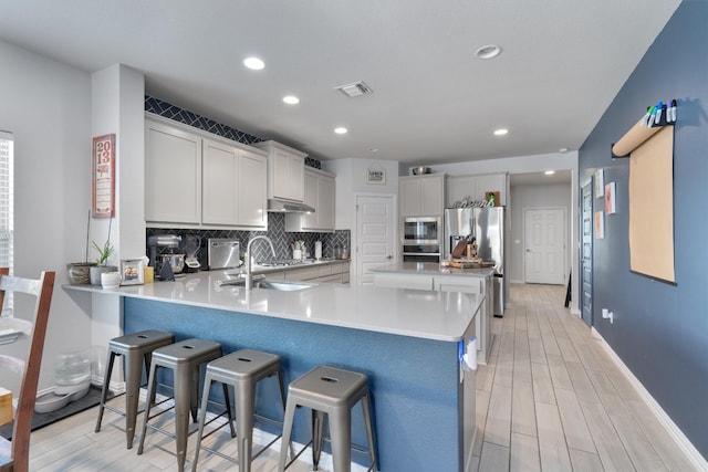 kitchen with light wood-type flooring, appliances with stainless steel finishes, sink, a breakfast bar, and kitchen peninsula