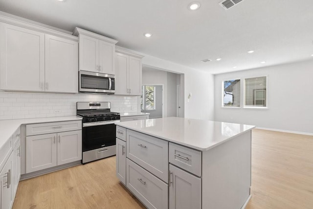 kitchen featuring gray cabinetry, stainless steel appliances, tasteful backsplash, light hardwood / wood-style flooring, and a kitchen island