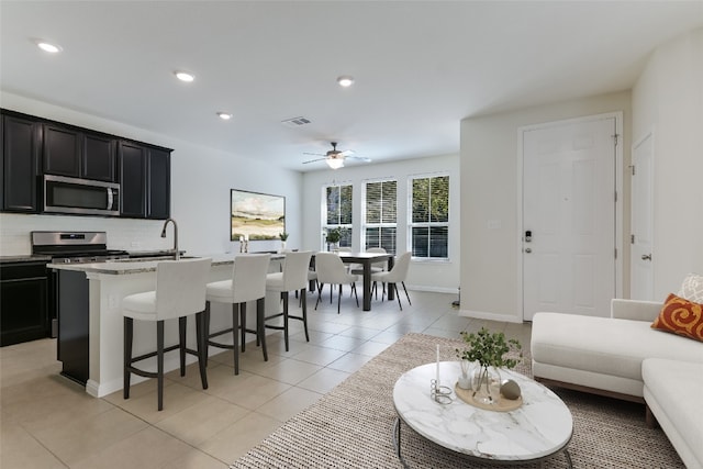 kitchen with a center island with sink, ceiling fan, light tile patterned floors, appliances with stainless steel finishes, and tasteful backsplash