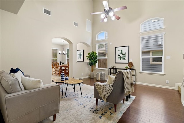 living room featuring wood-type flooring, ceiling fan with notable chandelier, and a towering ceiling