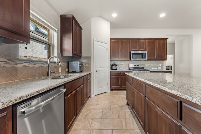 kitchen with sink, light stone countertops, appliances with stainless steel finishes, tasteful backsplash, and dark brown cabinets