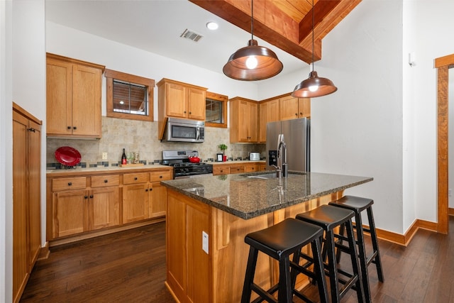 kitchen featuring stainless steel appliances, dark stone countertops, an island with sink, dark wood-type flooring, and pendant lighting