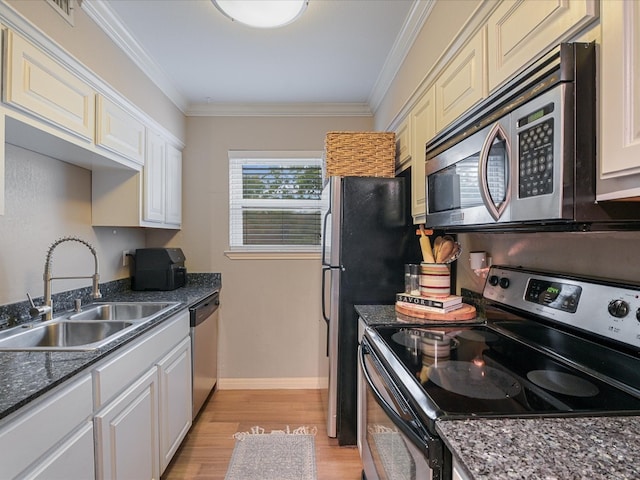 kitchen with sink, ornamental molding, light wood-type flooring, appliances with stainless steel finishes, and dark stone countertops