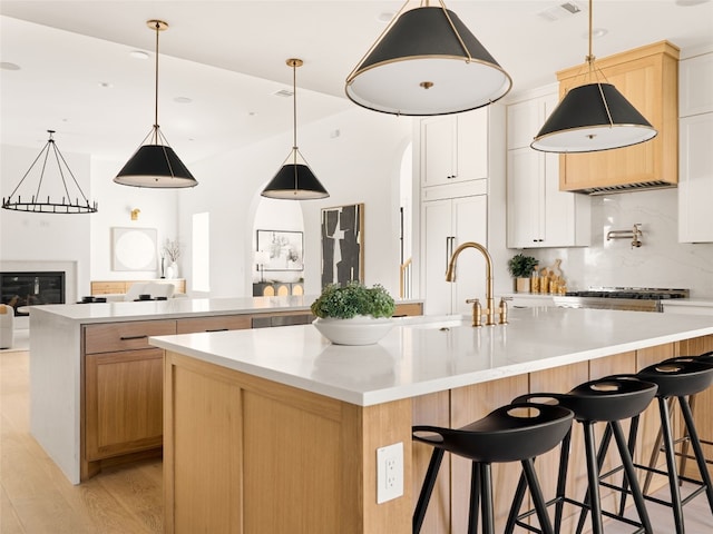 kitchen with tasteful backsplash, a large island with sink, white cabinets, and hanging light fixtures