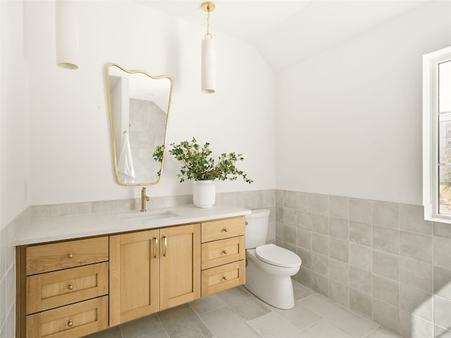 bathroom featuring tile patterned floors, vaulted ceiling, toilet, vanity, and tile walls