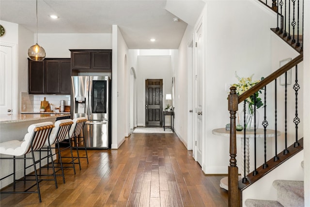 kitchen with decorative light fixtures, dark brown cabinetry, dark hardwood / wood-style flooring, a breakfast bar, and stainless steel fridge