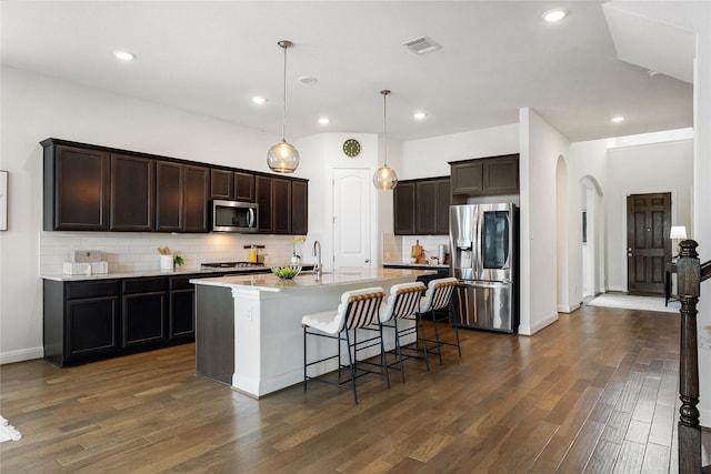 kitchen featuring pendant lighting, an island with sink, a breakfast bar, tasteful backsplash, and appliances with stainless steel finishes