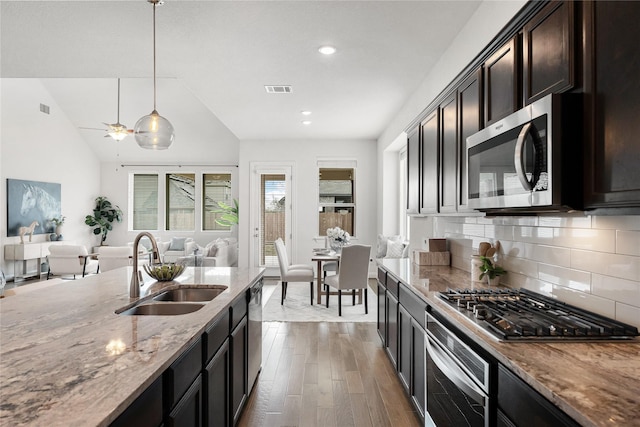 kitchen with stainless steel appliances, sink, light stone countertops, dark hardwood / wood-style flooring, and pendant lighting