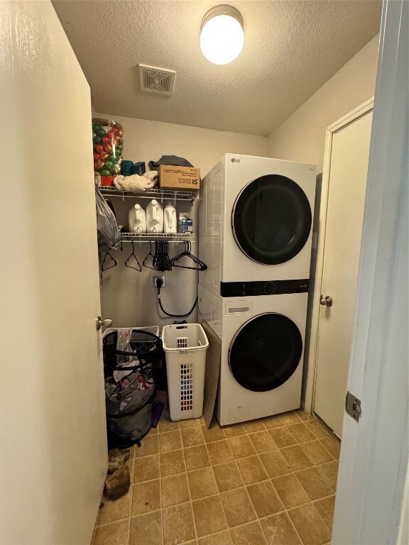 laundry room featuring stacked washer and clothes dryer and a textured ceiling