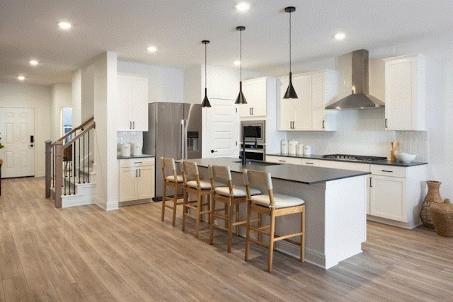 kitchen with an island with sink, a kitchen bar, wall chimney exhaust hood, and light hardwood / wood-style floors