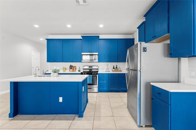 kitchen featuring light tile patterned flooring, a kitchen island with sink, appliances with stainless steel finishes, and blue cabinets