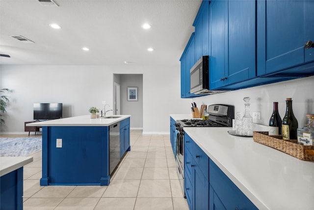 kitchen featuring light tile patterned flooring, a center island with sink, stainless steel appliances, blue cabinetry, and sink