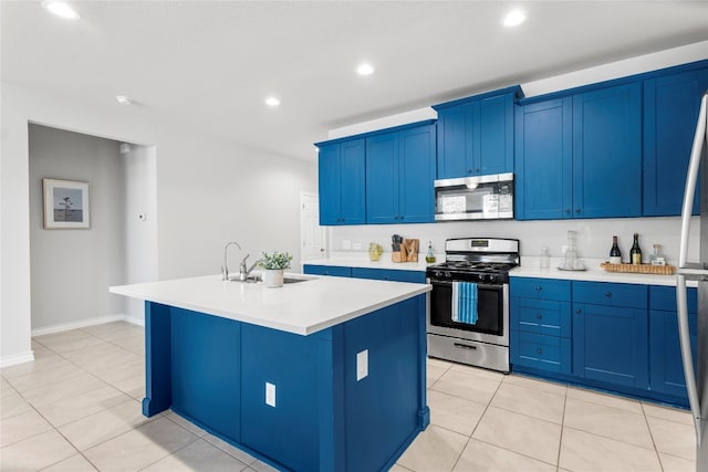 kitchen featuring sink, appliances with stainless steel finishes, light tile patterned floors, blue cabinetry, and a kitchen island with sink