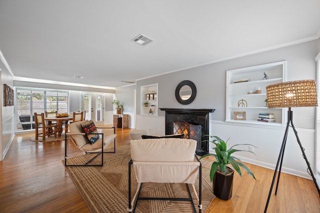 living room with hardwood / wood-style floors, built in shelves, and crown molding