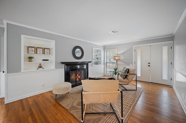 living room featuring built in features, hardwood / wood-style flooring, and crown molding