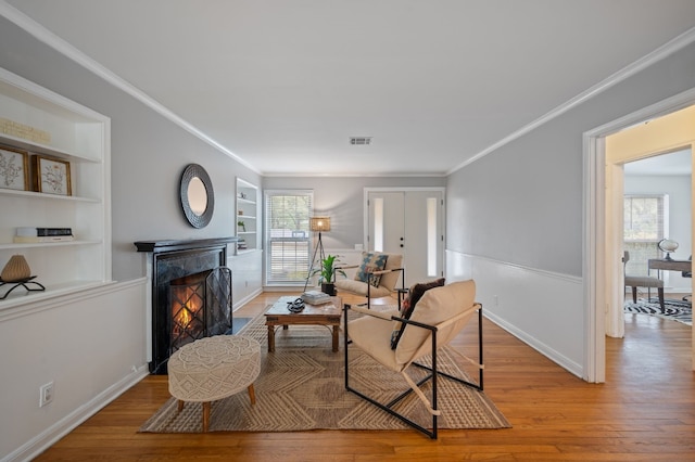 living room with a wealth of natural light, light hardwood / wood-style floors, built in shelves, and ornamental molding