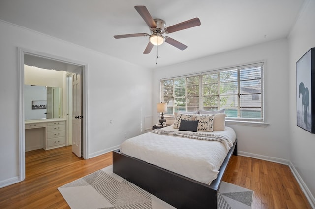 bedroom featuring wood-type flooring, built in desk, ceiling fan, and ensuite bath