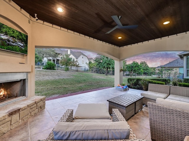 patio terrace at dusk with an outdoor living space with a fireplace, a yard, and ceiling fan