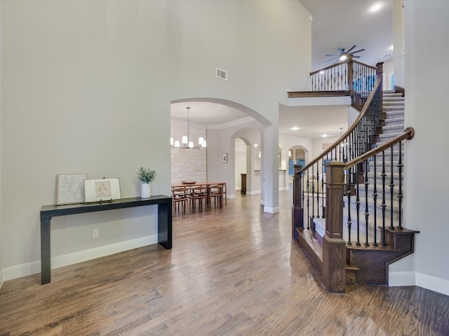 entryway with wood-type flooring, ceiling fan with notable chandelier, and a towering ceiling